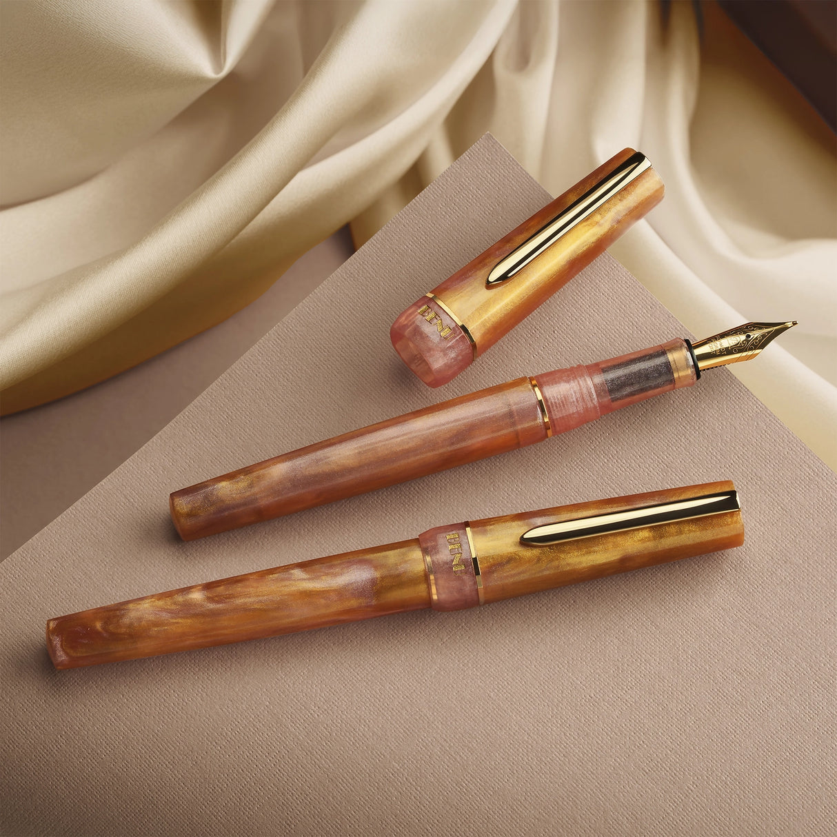 BENU presents the newest Haute Collection — a line of elegant, fashion-inspired pens that blend classic charm with bold, modern flair. The designs include both subtle and vibrant styles, showcasing BENU’s signature glitter and color artistry. Each pen features a faceted body with alternating wide and slender facets, complemented by either gold-plated or chrome-plated trims for a sleek, timeless look.
Lustre pen glows with warm swirls of amber and blush, finished in radiant gold trim.Quietly luxurious, Lust