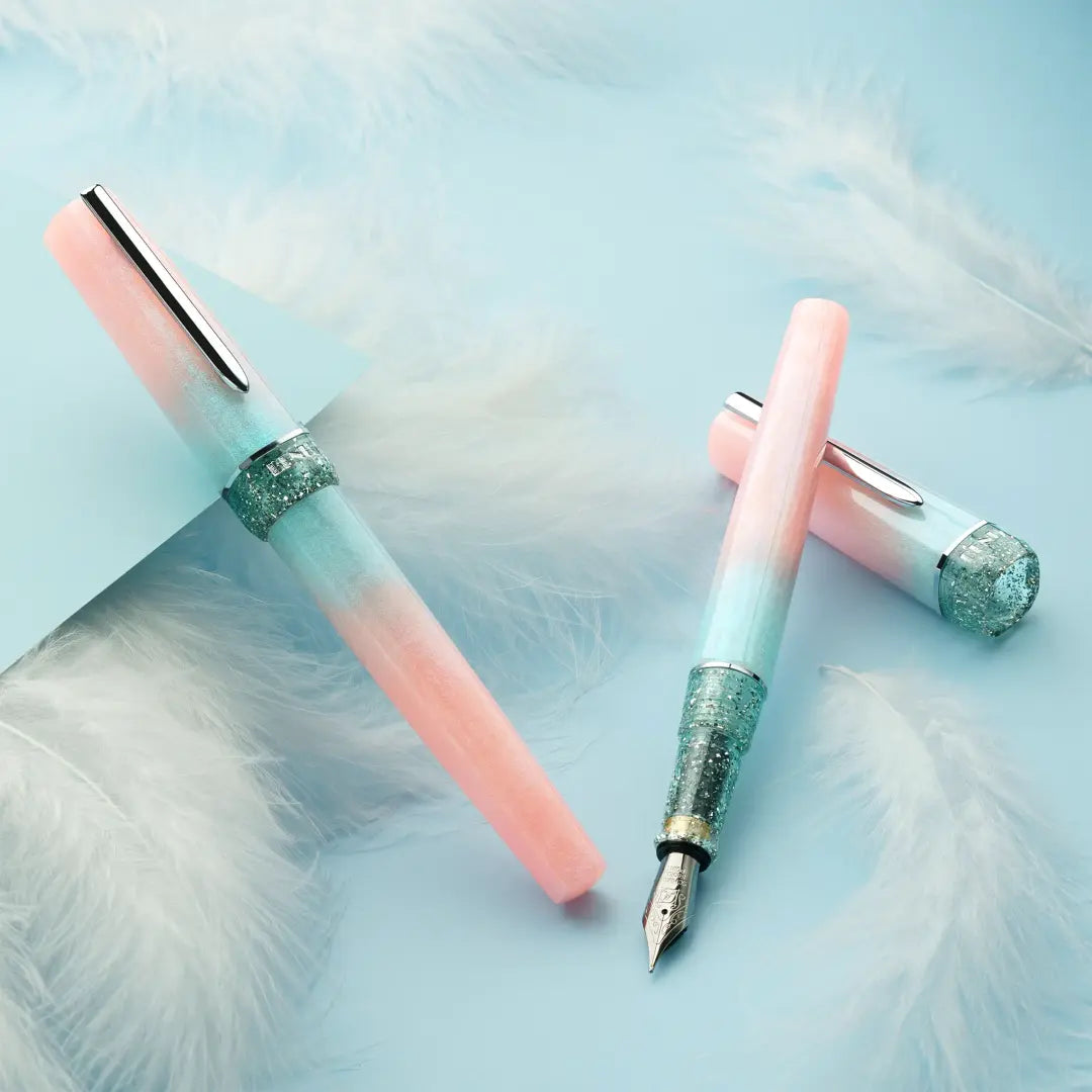 BENU presents the newest Haute Collection — a line of elegant, fashion-inspired pens that blend classic charm with bold, modern flair. The designs include both subtle and vibrant styles, showcasing BENU’s signature glitter and color artistry. Each pen features a faceted body with alternating wide and slender facets, complemented by either gold-plated or chrome-plated trims for a sleek, timeless look.
Soft shades of rose and mint melt together in Perle, accented by a sparkling band. As fresh as spring light