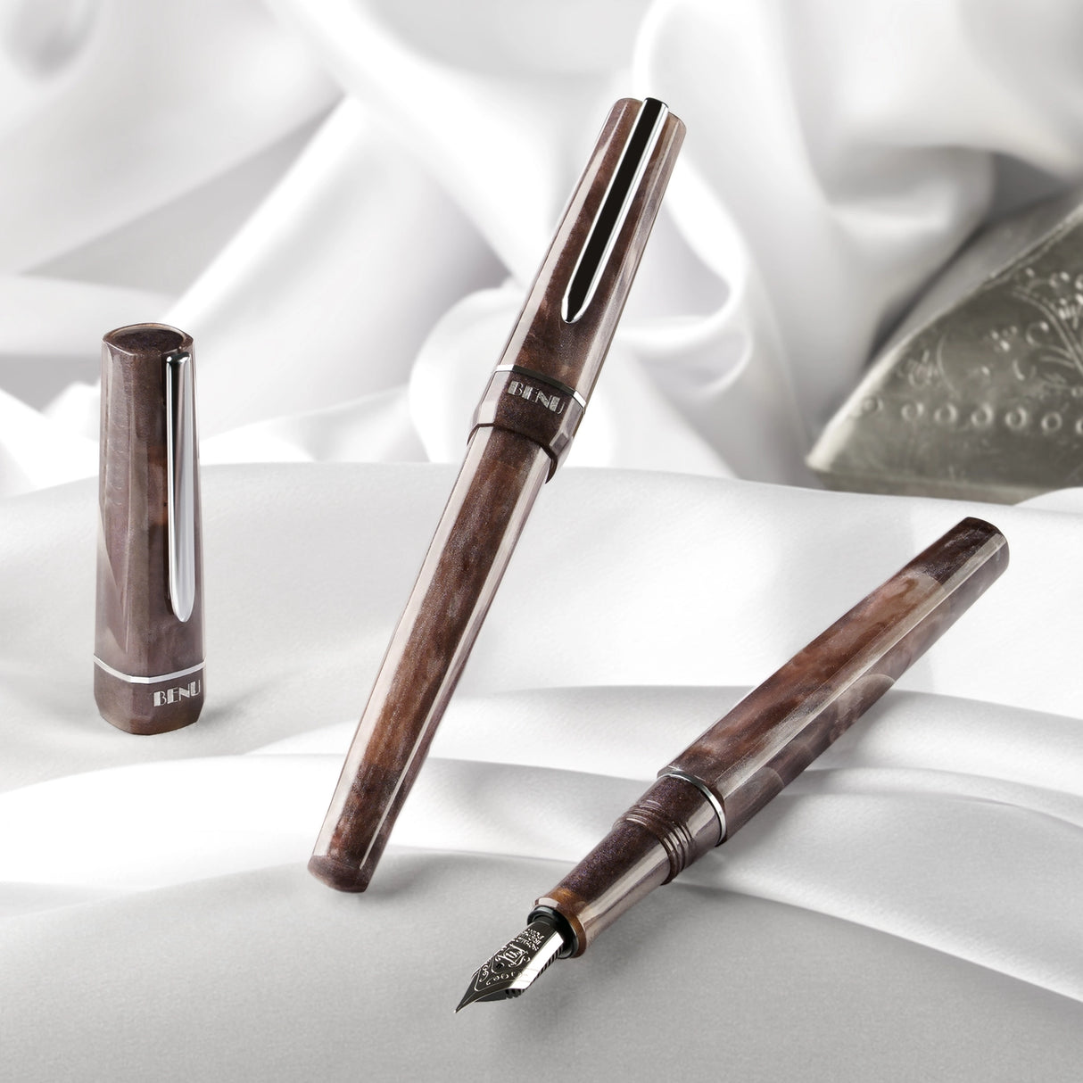 BENU presents the newest Haute Collection — a line of elegant, fashion-inspired pens that blend classic charm with bold, modern flair. The designs include both subtle and vibrant styles, showcasing BENU’s signature glitter and color artistry. Each pen features a faceted body with alternating wide and slender facets, complemented by either gold-plated or chrome-plated trims for a sleek, timeless look.
With smoky gray marbling and polished chrome hardware, Satin is the essence of modern elegance. Understated