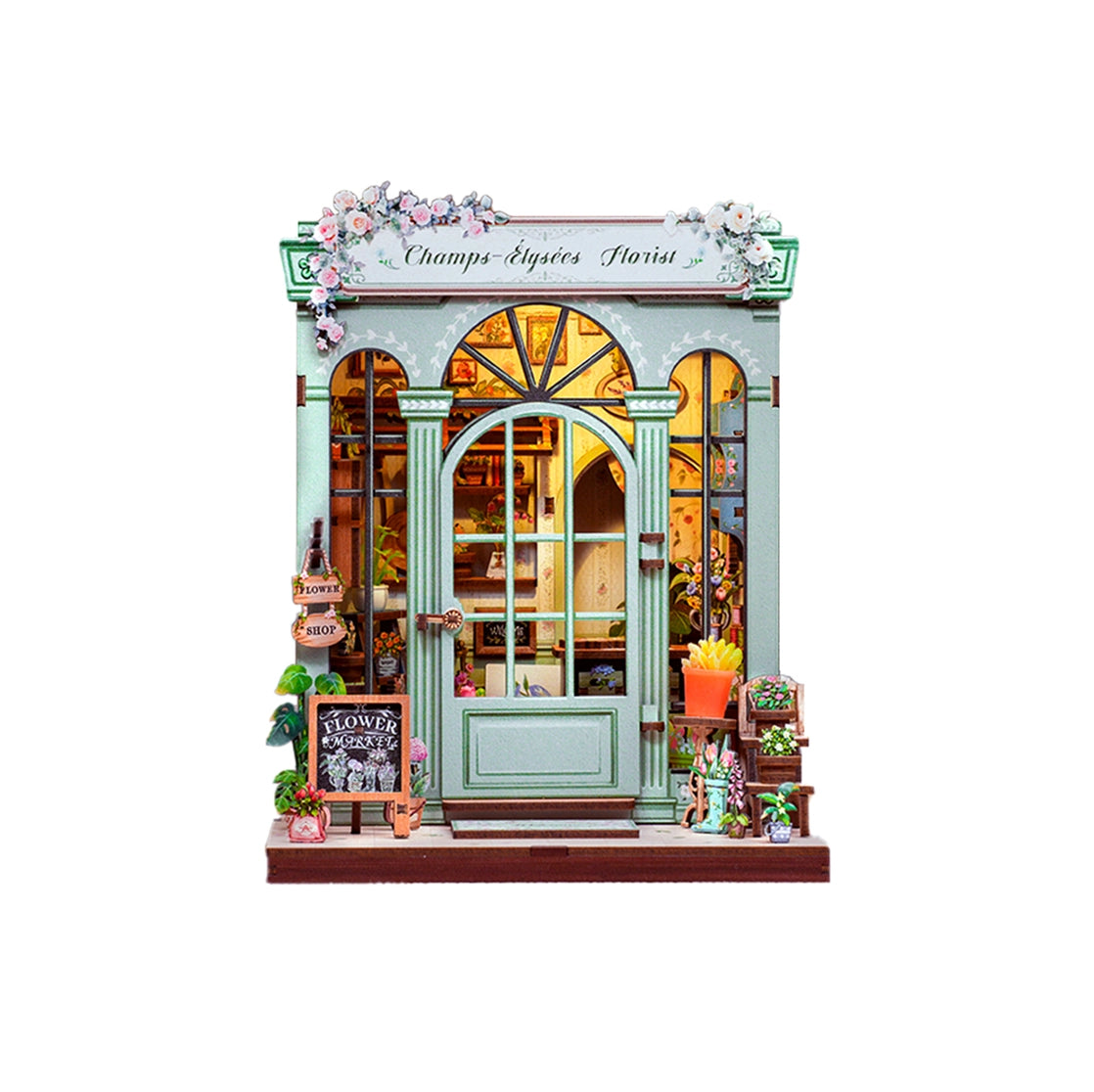 This elegant miniature captures the beauty of a boutique flower shop, adorned with delicate blooms, pastel accents, and a graceful arched doorway that invites you inside.
From the dainty floral arrangements to the hand-painted shop signs and warm, glowing interior, every detail evokes the feeling of strolling down the Champs-Élysées on a sunny afternoon. The soft LED lights cast a welcoming glow, highlighting rows of flowers ready to be wrapped for someone special.