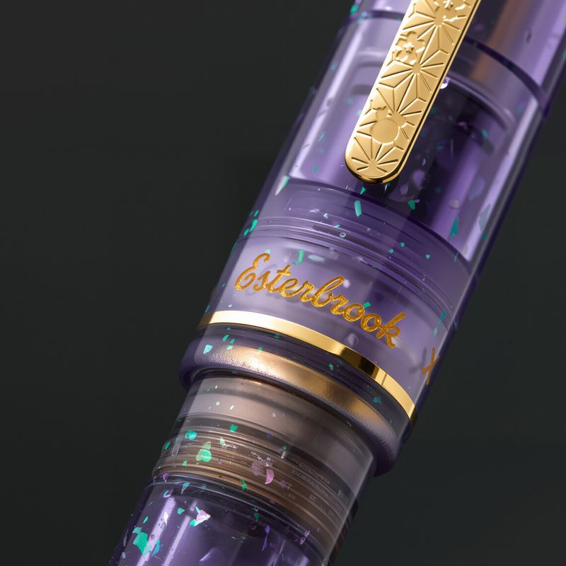Esterbrook x Sakuradragon Sakura Street Estie Fountain Pen
Created with artist Cindy Duong of Sakuradragon, the Sakura Street Estie brings her imaginative illustrated world to Esterbrook's traditional Estie fountain pen. Its U.S.-blended material combines translucent purple with colorful glitter sparkle, while the custom clip is etched with Cindy's Sakura pattern. Dual Esterbrook and Sakuradragon engraving and a gold-plated converter finish the design. Each pen arrives in special packaging with Japanese gi
