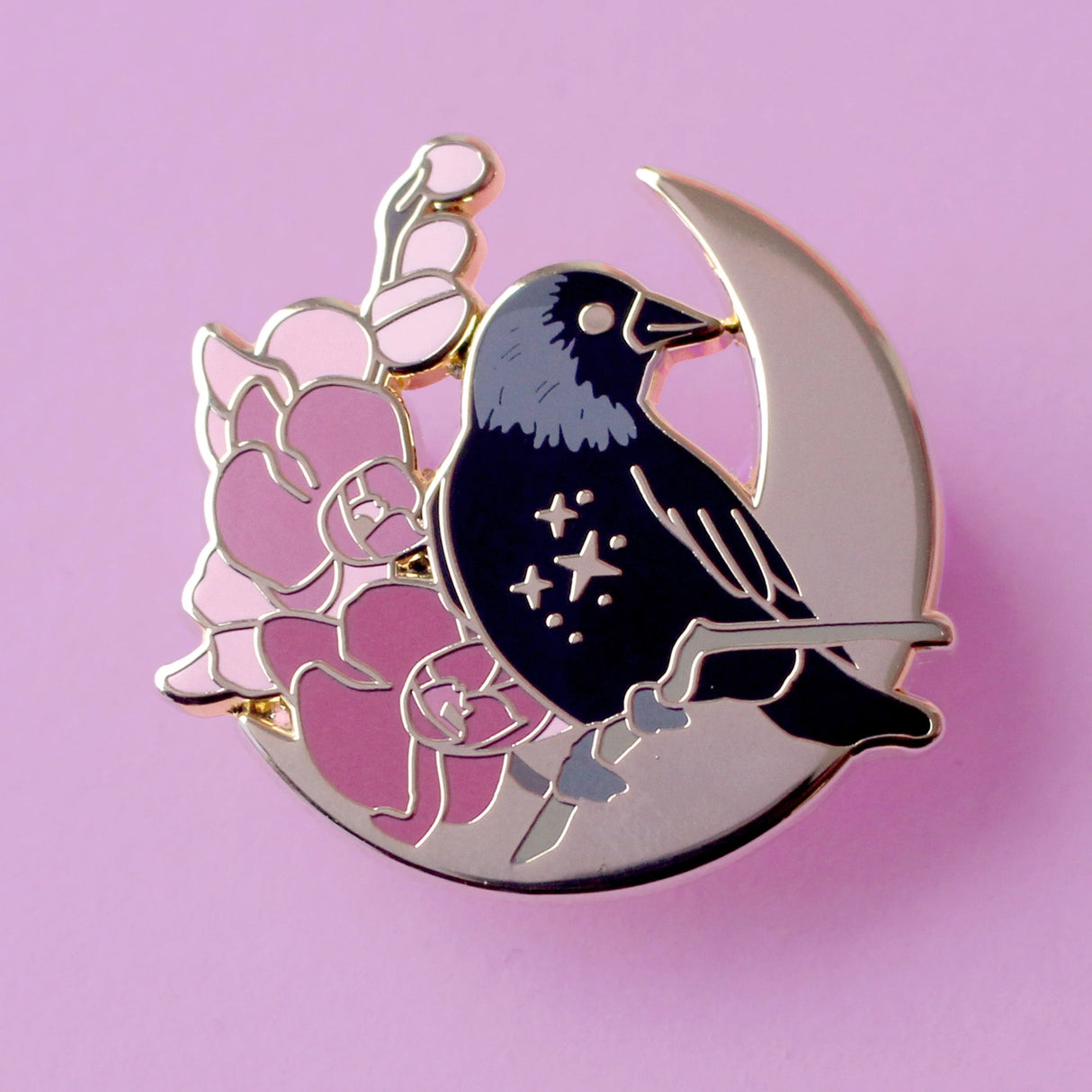 This enamel pin features a Jackdaw perching on a branch of pink orchid flowers, in front of a large gold moon. The pin is presented on a Glitter Punk backing card and is secured with 2 pin backs.
This pin is part of the Corvid Collection, an 8-part series of bird pins.
Measurements: 35mm