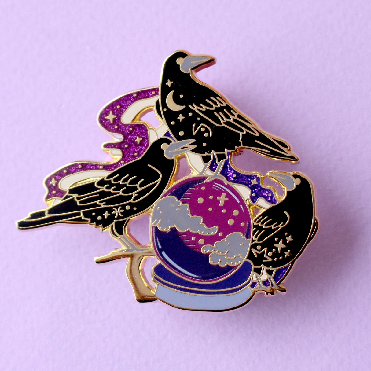 This enamel pin features three rooks sitting around a crystal ball, surrounded by glittery mystical smoke trails. The pin is presented on a Glitter Punk backing card and is secured with 2 pin backs.
This pin is part of the Corvid Collection, an 8-part series of bird pins.
Measurements: 54mm