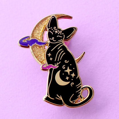 Cute, cuddly and clever – there’s no cat quite like a Sphynx! This fab enamel pin features a black Sphynx covered in mystical symbols, sitting in front of a crescent moon with 2 purple clouds.
The pin is 42mm (1.65”) tall, and is made from gunmetal hard enamel, with glitter and UV printed details. It's secured with 2 pink clutches to keep the pin in place.