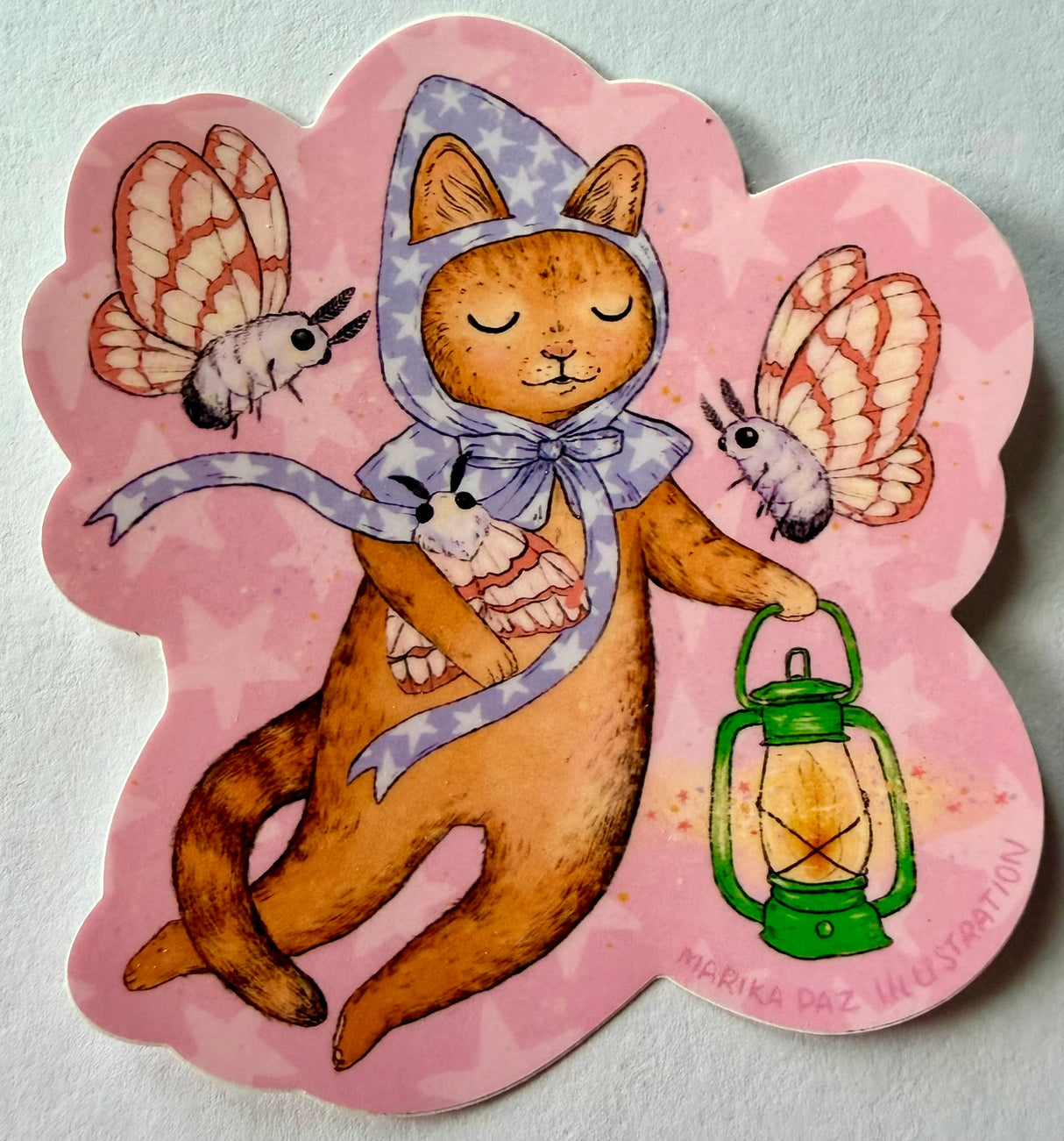 A cat and his lantern attract moths as they float amongst the stars.
This vinyl matte sticker is weather and waterproof-stick it on a notebook, bike, or car- it's going to stick around! Heck, throw it on a water bottle and through the dishwasher. This sticker can go anywhere. Sticker measures 3.5" x 4.5" Printed in USA.