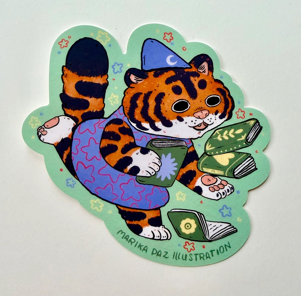 This tiger loves books so much, she can't hold them all at once!
This vinyl matte sticker is weather and waterproof-stick it on a notebook, bike, or car- it's going to stick around! Heck, throw it on a water bottle and through the dishwasher. This sticker can go anywhere. Sticker measures 4" x 4" Printed in USA.