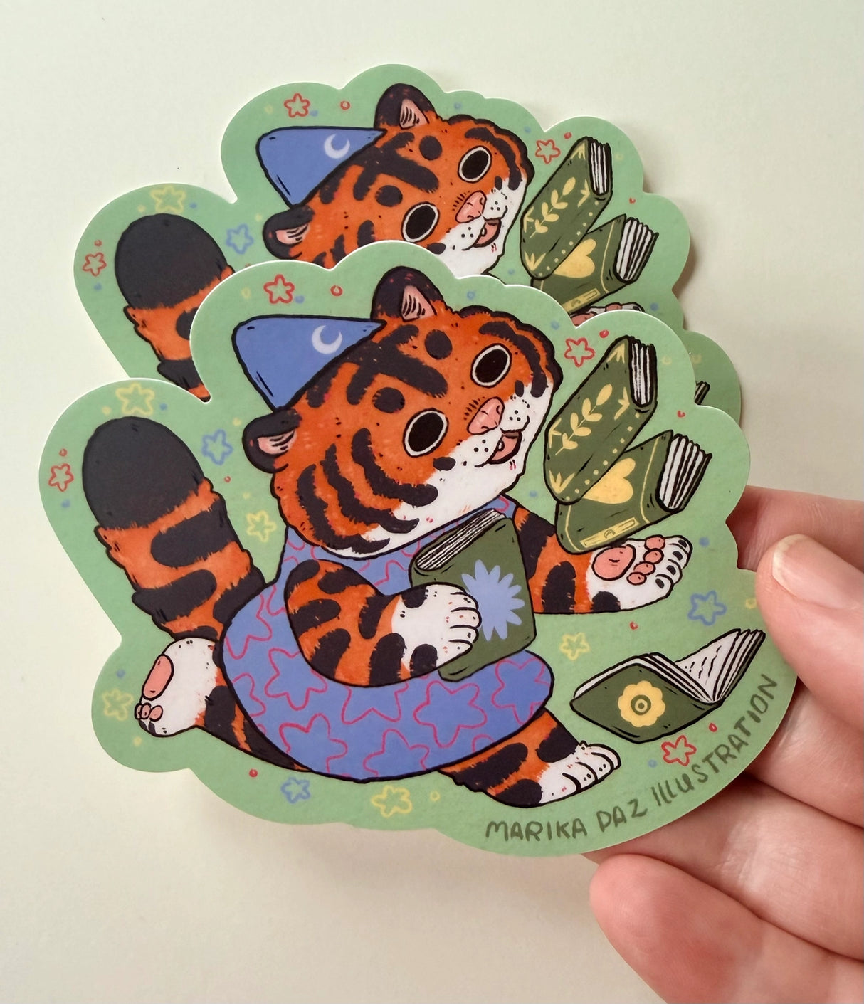 This tiger loves books so much, she can't hold them all at once!
This vinyl matte sticker is weather and waterproof-stick it on a notebook, bike, or car- it's going to stick around! Heck, throw it on a water bottle and through the dishwasher. This sticker can go anywhere. Sticker measures 4" x 4" Printed in USA.
