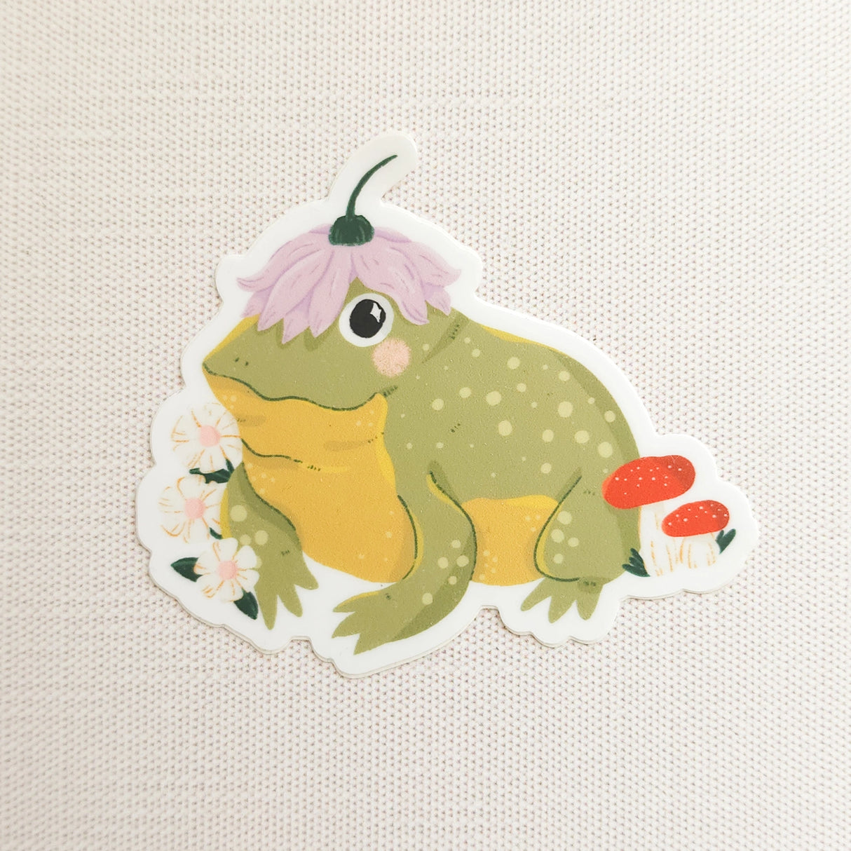 A happy little toad pauses among blooming flowers and mushrooms, a small flower worn proudly atop his head. This vinyl sticker captures that lighthearted moment, celebrating comfort, confidence, and being yourself in the everyday.
Made from durable, waterproof vinyl, this sticker is designed to hold up wherever you place it—whether that’s a water bottle, laptop, or journal you reach for daily.