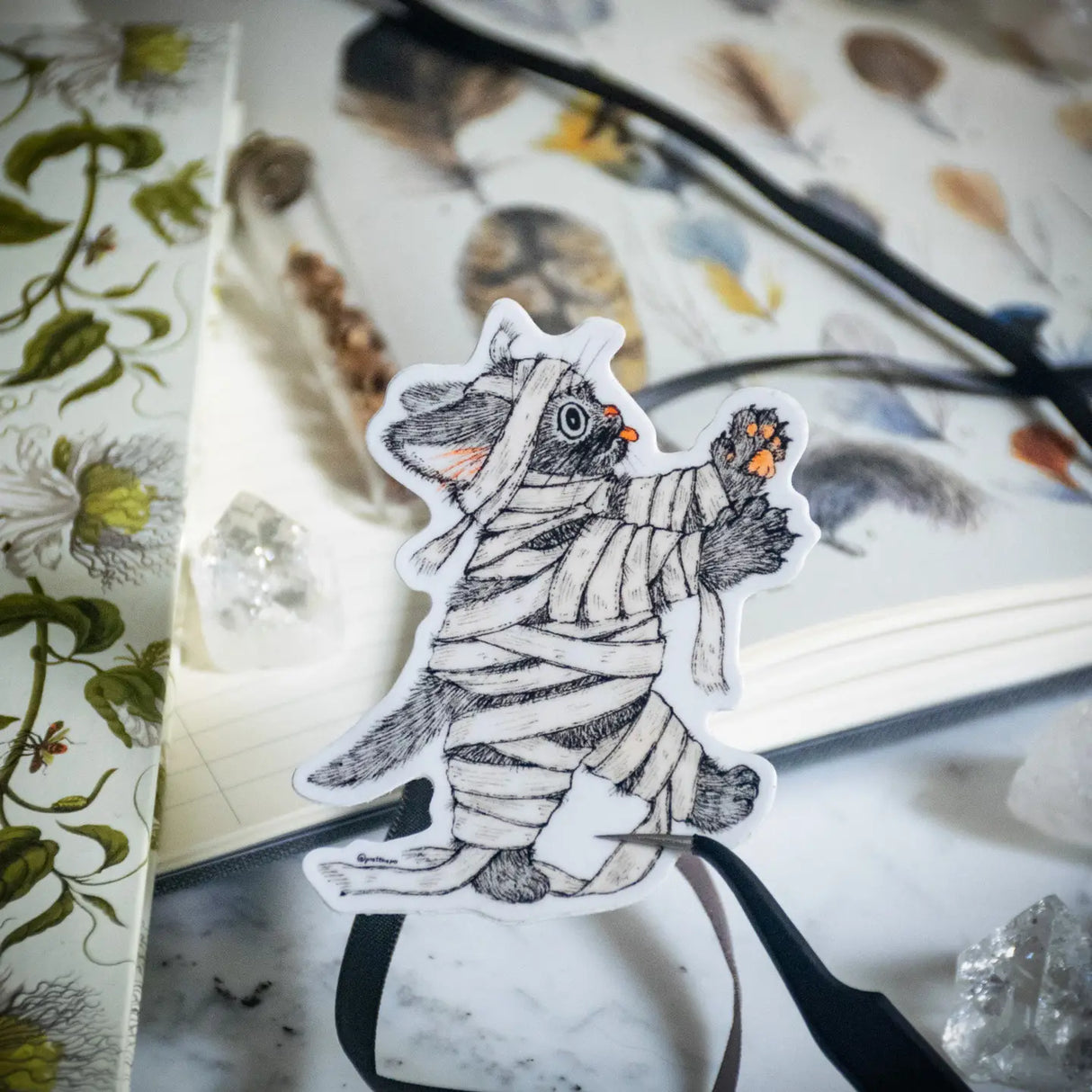 This cute little kitty has morphed into a walking zombie on the hunt. Illustrated in a whimsical pen-and-ink style with a soft vintage touch, “Zombie Kitty” brings a spooky charm and a smile wherever it goes. Printed on durable white vinyl, this sticker is waterproof, UV-proof, and long-lasting — perfect for decorating water bottles, laptops, journals, or anywhere a touch of magic is needed.