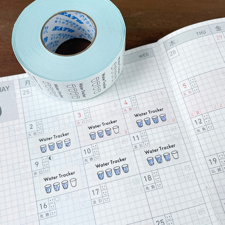 Stamp Marche Planner Label Sticker Roll - Water Tracker Roll of tape with water tracker labels on a calendar page