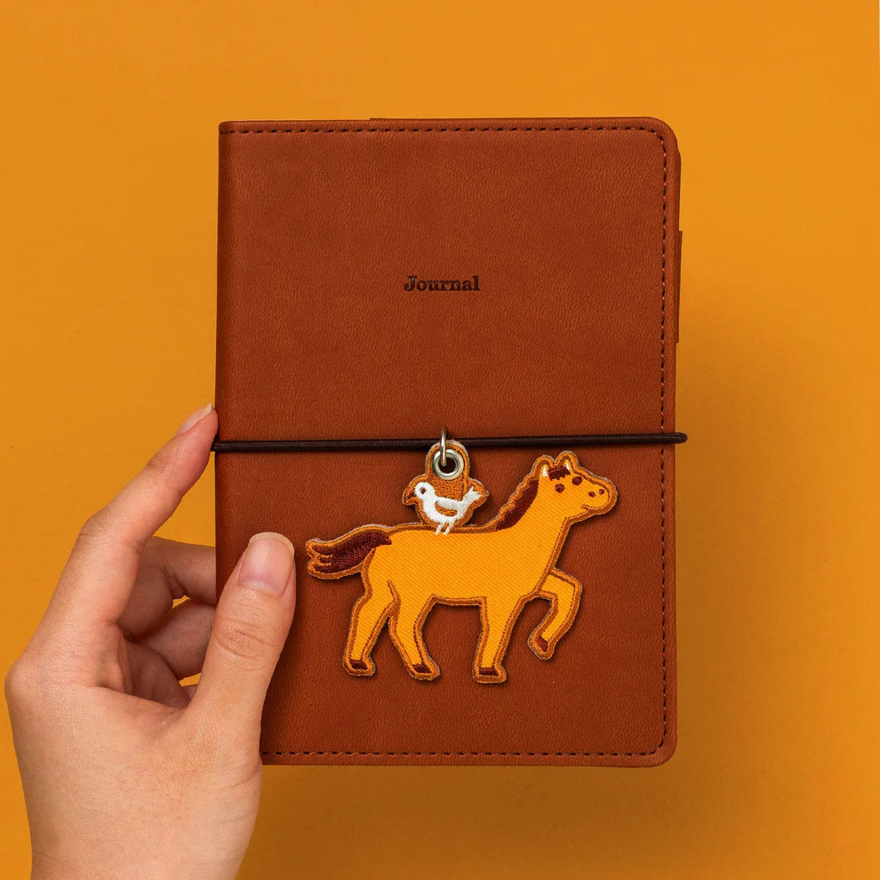 An embroidery keychain featuring the Horse which is the seventh sign of the Chinese zodiac. The horse symbolizes vitality and bold changes. Get lucky to use it as a keychain and a tag for your planner. LNY is February 17th this year!
A little bird perched atop on the brown horse adds a charming accent. The back side is embroidered with the word "uma" in hiragana, meaning a horse in Japanese. 