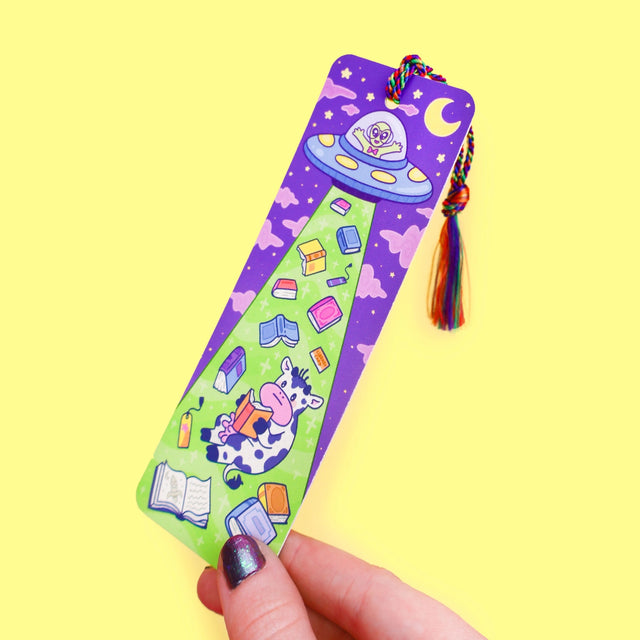 'Alien Abduction Bookmark by Turtle's Soup. Libraries beware! This nerdy alien is abducting every book in town! He loves reading the unique stories that fill planet Earth. His abduction beam has a wide range, so he might accidentally pick up some life forms as well. Hopefully, they don’t mind reading among the stars with him!

Hold your spot in style with our fun and funky bookmark collection! Whether you prefer romance, fantasy, or science fiction, our bookmarks will fit perfectly between the pages of your