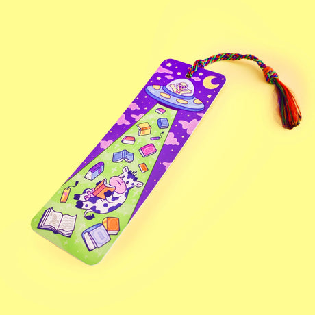 'Alien Abduction Bookmark by Turtle's Soup. Libraries beware! This nerdy alien is abducting every book in town! He loves reading the unique stories that fill planet Earth. His abduction beam has a wide range, so he might accidentally pick up some life forms as well. Hopefully, they don’t mind reading among the stars with him!

Hold your spot in style with our fun and funky bookmark collection! Whether you prefer romance, fantasy, or science fiction, our bookmarks will fit perfectly between the pages of your