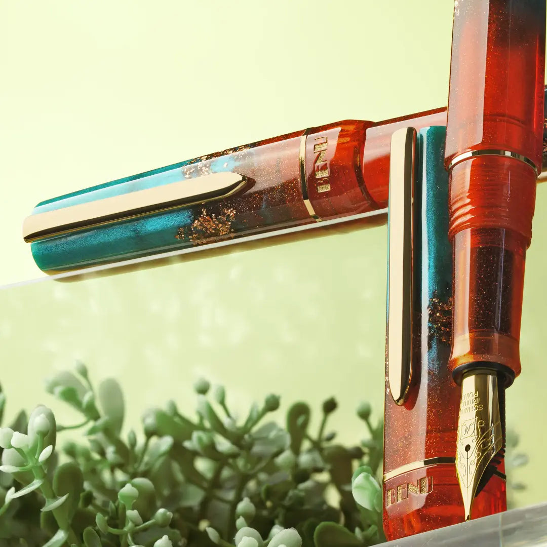 BENU presents the newest Haute Collection — a line of elegant, fashion-inspired pens that blend classic charm with bold, modern flair. The designs include both subtle and vibrant styles, showcasing BENU’s signature glitter and color artistry. Each pen features a faceted body with alternating wide and slender facets, complemented by either gold-plated or chrome-plated trims for a sleek, timeless look.

With a bold orange and teal body streaked with gold, Chic turns heads with runway-ready style. Fashion-forw