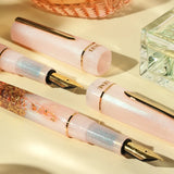 BENU presents the newest Haute Collection — a line of elegant, fashion-inspired pens that blend classic charm with bold, modern flair. The designs include both subtle and vibrant styles, showcasing BENU’s signature glitter and color artistry. Each pen features a faceted body with alternating wide and slender facets, complemented by either gold-plated or chrome-plated trims for a sleek, timeless look.

A mix of golden flakes dances through a soft, pearly pink base, complemented by gleaming gold trim. Tender 
