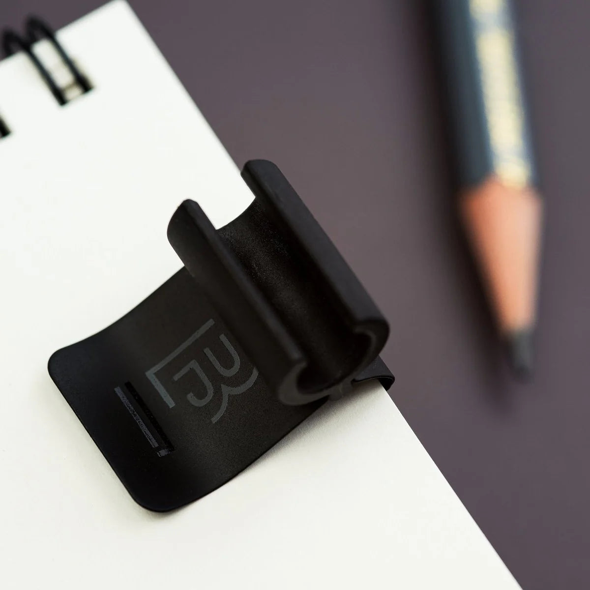 The Blackwing Notebook Clip is designed to keep your pencil and paper together. The clip is made of aluminum and finished with our signature matte black texture. Once you attach the reusable clip to your notebook, your pencil snaps into a durable thermoplastic polymer that won't scuff the lacquer. Perfect for everyday carry—clip it onto your spiral notebook, legal pad, memo book, or reading book to keep your stationery organized.
