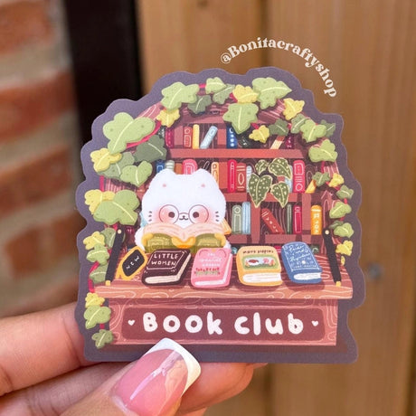 Join the cutest book club around with this Book Club Cat Sticker! Surrounded by stacks of classic books, this cozy cat with glasses is the perfect reading buddy for bookworms and cat lovers alike. This kawaii library sticker captures a warm, cottagecore aesthetic with leafy vines, wooden shelves, and soft colors that make it feel like a mini reading nook. Ideal for adding charm to your laptop, water bottle, journal, Kindle, or planner.

♡ STICKER DETAILS ♡
~ Sticker size: 2.5’’ inches
~ Printed on matte sti