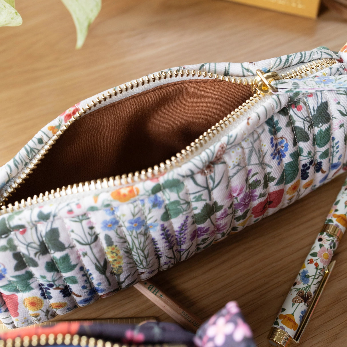 Each versatile pouch showcases premium quilted cotton in four distinct illustrated patterns, complemented by an elegant gold brass zipper with coordinating pull—adding a sophisticated finishing touch to these signature pieces.

Features:

Size: 7" x 3" x 2"
Premium quilted cotton exterior
Coordinating interior cotton lining
Gold brass zipper with matching pull
Versatile use as pencil pouch or makeup bag
Perfect for desk display or on-the-go organization