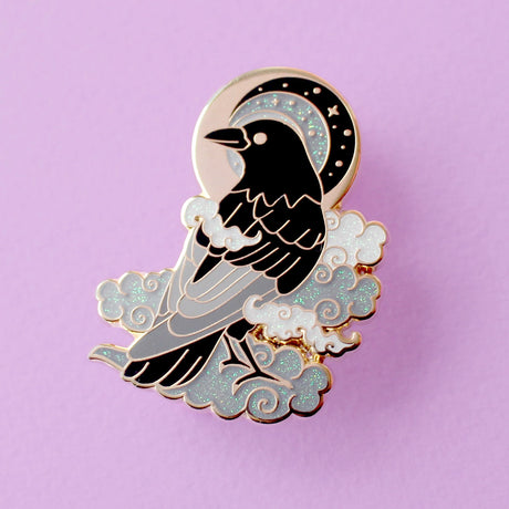 This enamel pin features a black crow surrounded by grey glittery clouds, and a starry moon with grey backgrounds. The pin is presented on a Glitter Punk backing card and is secured with 2 pin backs.

This pin is part of the Corvid Collection, an 8-part series of bird pins.&nbsp;

Measurements: 39mm