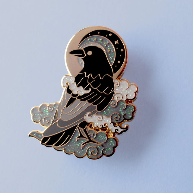 This enamel pin features a black crow surrounded by grey glittery clouds, and a starry moon with grey backgrounds. The pin is presented on a Glitter Punk backing card and is secured with 2 pin backs.

This pin is part of the Corvid Collection, an 8-part series of bird pins.&nbsp;

Measurements: 39mm