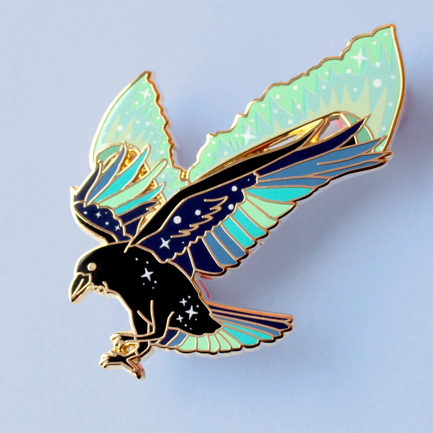 This enamel pin features a raven with its wings outstretched and the northern lights fanning out behind it. The pin is presented on a Glitter Punk backing card and is secured with 2 pin backs.

This pin is part of the Corvid Collection, an 8-part series of bird pins. 

Measurements: 46mm