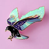 This enamel pin features a raven with its wings outstretched and the northern lights fanning out behind it. The pin is presented on a Glitter Punk backing card and is secured with 2 pin backs.

This pin is part of the Corvid Collection, an 8-part series of bird pins. 

Measurements: 46mm