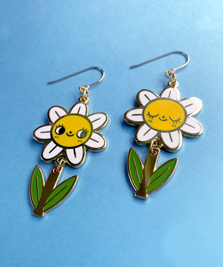 A pair of mis-matched happy daisy themed earrings (one one with happy open eyes, and one with happy closed) with separate dangling stems. Made from hard enamel with shiny gold metal finish on high quality Hypo-Allergenic, gold plated, brass based hooks.

Each earring measures approximately 5cm tall x 3cm wide. Earrings come in a Hannakin embossed gift box.