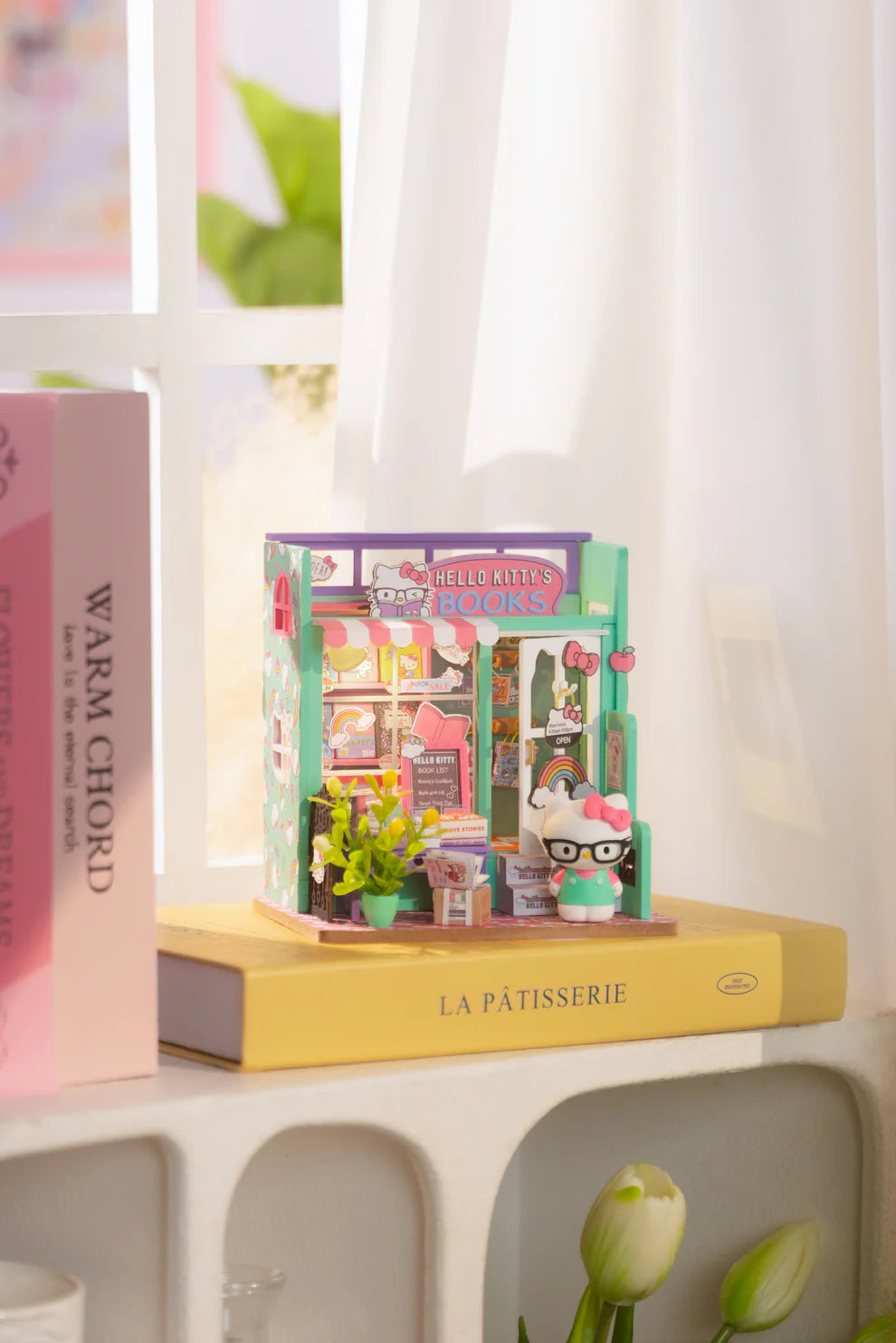 Step into the charming world of Hello Kitty with this delightful miniature house kit, where she runs her very own bookstore. Filled with tiny books, adorable gifts, and colorful gift bags, this kit is decorated in Hello Kitty's iconic style. The charming "open" sign welcomes you into the cozy shop, where a little lamp lights up the interior, creating a warm and inviting atmosphere. Perfect for fans and crafters alike, this kit offers hours of fun and a beautiful keepsake to treasure.