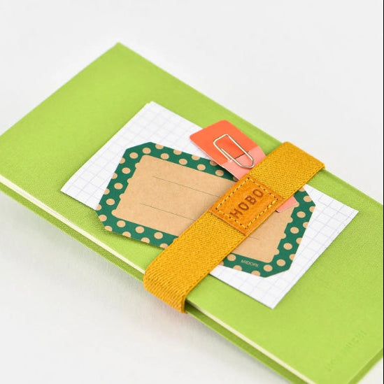 Handy for keeping your book shut in your bag, this bookband is made with an elastic band adorned with the Hobonichi “Hobo” logo. There are two different holes to fit the clasp so you can still use it if your book becomes thicker.

Included in the bookband are slots to store two pens, and the bands come in six colors. (Classic uses natural leather and will grow darker over continued use.)