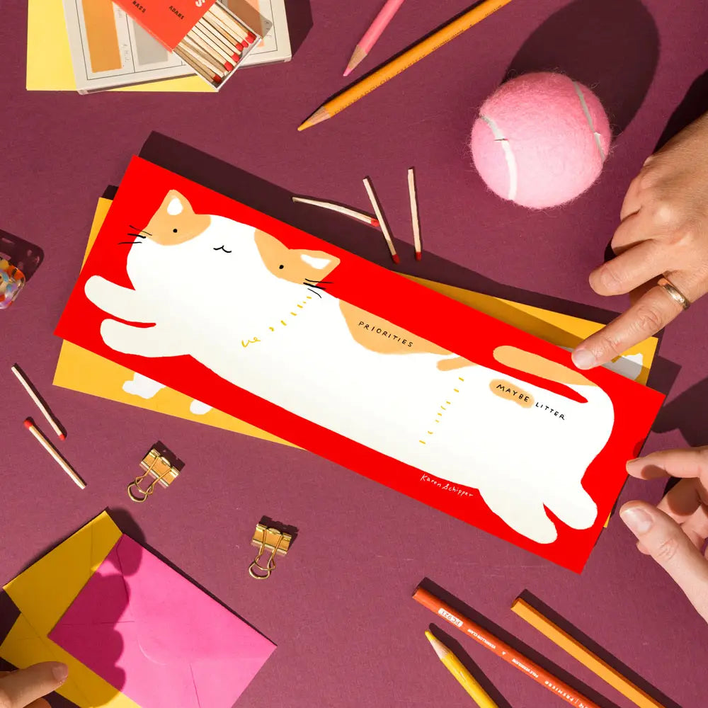 Karen Schipper Weekly Desk Planner - Cooper Cat

Planning doesn’t have to feel serious. Cooper Cat Desk Planner is a cat desk planner pad featuring a chubby white cat stretched across a bold red background with the playful sections “Priorities” and “Maybe Later” — a cute cat planner that instantly catches attention.

It comes with 52 undated sheets, enough to last you the year.
Professionally printed full color
Size: 11.75 x 4.25 inches
52 tear-off sheets with cardboard backing
Packaged in plastic sleeve an
