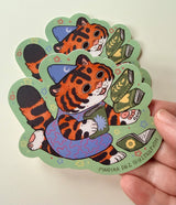 This tiger loves books so much, she can't hold them all at once!

This vinyl matte sticker is weather and waterproof-stick it on a notebook, bike, or car- it's going to stick around! Heck, throw it on a water bottle and through the dishwasher. This sticker can go anywhere. Sticker measures 4" x 4" Printed in USA.