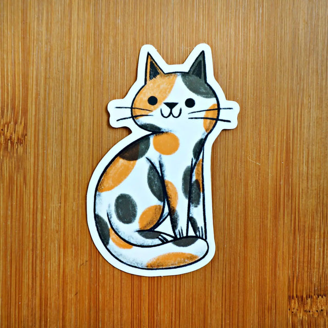 Sticker of a cat with orange and black spots on a wooden surface