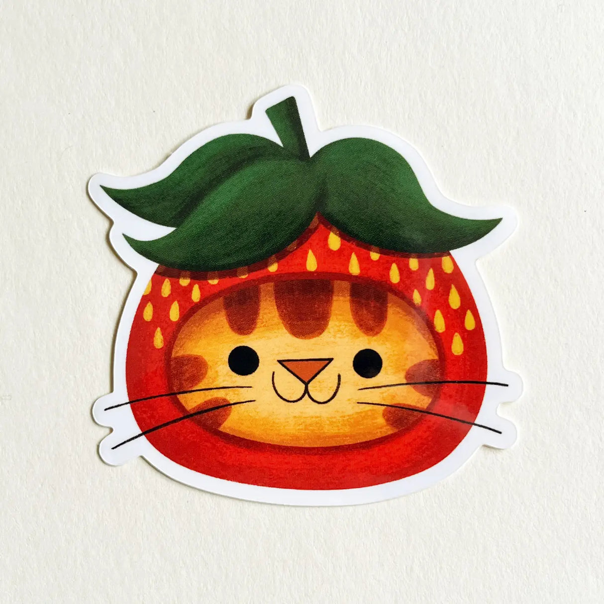 Sticker of a cat inside a strawberry with green leaves on a beige background
