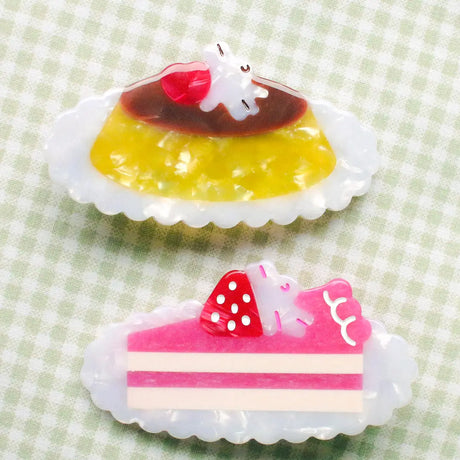 Pudding & Cake Hair Clips as a set of two clips. Clips are 2.5 inches long, made of acetate and have an alligator style clip on the back.

Clips should not be submerged in water.

Hair clips come with a backing card in a plastic sleeve.