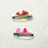 Pudding & Cake Hair Clips as a set of two clips. Clips are 2.5 inches long, made of acetate and have an alligator style clip on the back.

Clips should not be submerged in water.

Hair clips come with a backing card in a plastic sleeve.