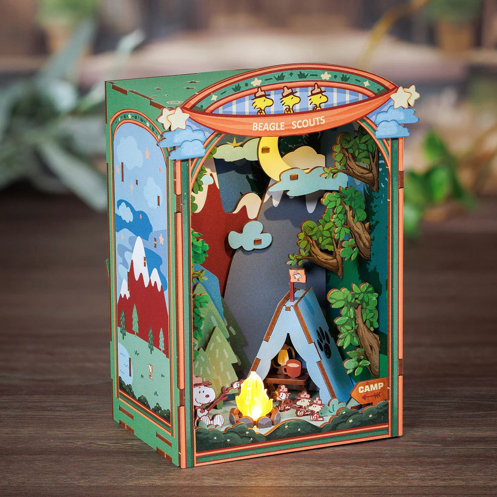 Gather 'round the campfire with Snoopy and his loyal Beagle Scouts in this heartwarming DIY Miniature Book Nook Kit! Nestled between trees and under the stars, Snoopy and the Woodstocks are toasting marshmallows over a crackling fire, their cozy tent pitched nearby. In the distance, gentle mountain silhouettes rise beyond the forest-setting the perfect scene for a peaceful, storybook escape.

This delightful book nook brings the charm of classic Peanuts adventures and the joy of outdoor camping into a beaut