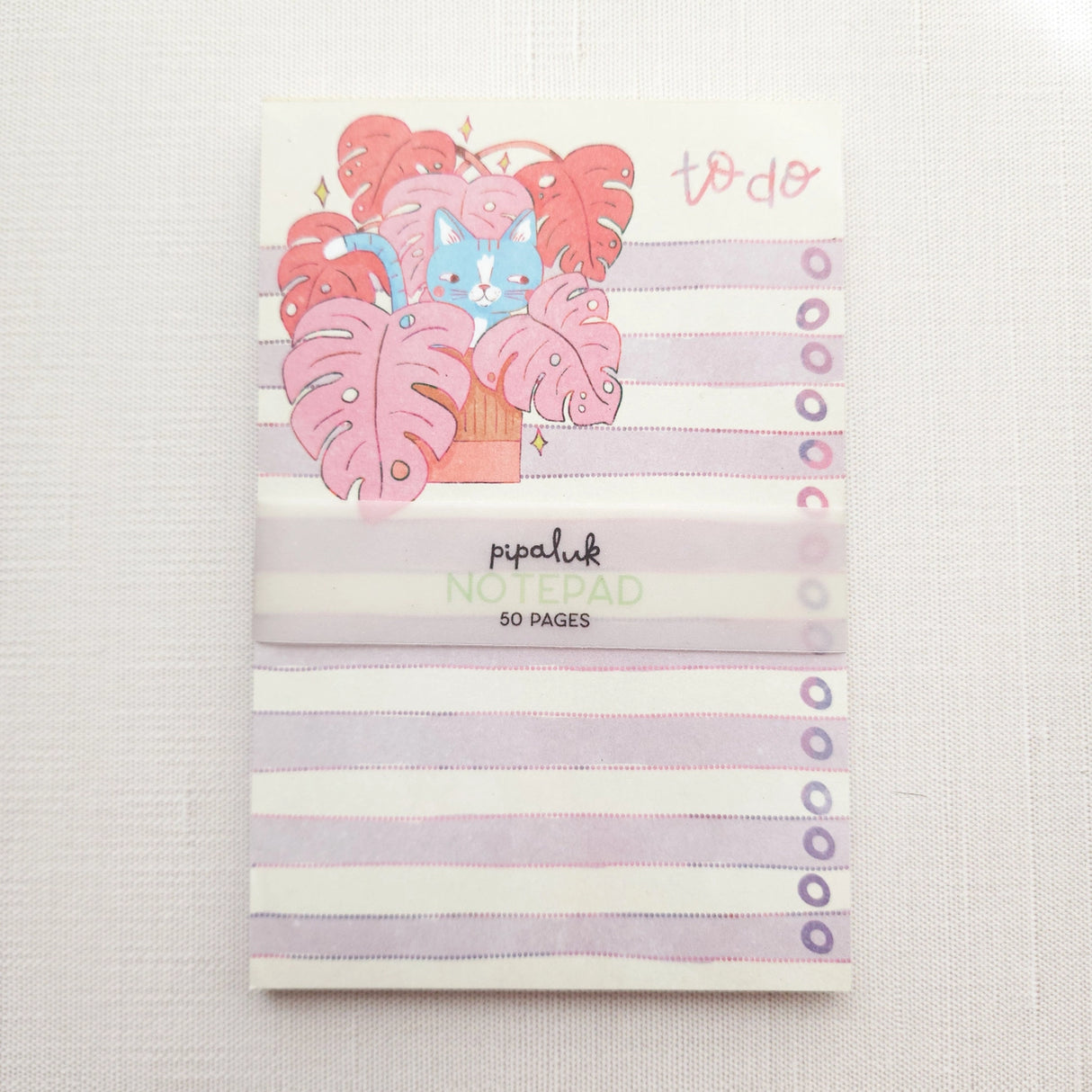 Inside a cozy Wildflower Woods cottage, a curious cat lounges among broad monstera leaves, tucked into a corner filled with filtered light and trailing greenery. This notepad brings that leafy, lived-in moment to your desk, making everyday lists feel a little more inviting.

Designed to be practical without feeling busy, this notepad offers a simple, cheerful way to keep track of daily to-do lists and planning.