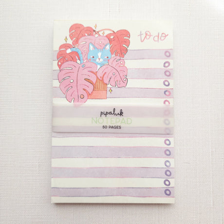 Inside a cozy Wildflower Woods cottage, a curious cat lounges among broad monstera leaves, tucked into a corner filled with filtered light and trailing greenery. This notepad brings that leafy, lived-in moment to your desk, making everyday lists feel a little more inviting.

Designed to be practical without feeling busy, this notepad offers a simple, cheerful way to keep track of daily to-do lists and planning.
