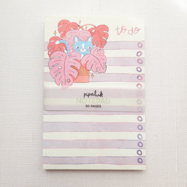 Inside a cozy Wildflower Woods cottage, a curious cat lounges among broad monstera leaves, tucked into a corner filled with filtered light and trailing greenery. This notepad brings that leafy, lived-in moment to your desk, making everyday lists feel a little more inviting.

Designed to be practical without feeling busy, this notepad offers a simple, cheerful way to keep track of daily to-do lists and planning.
