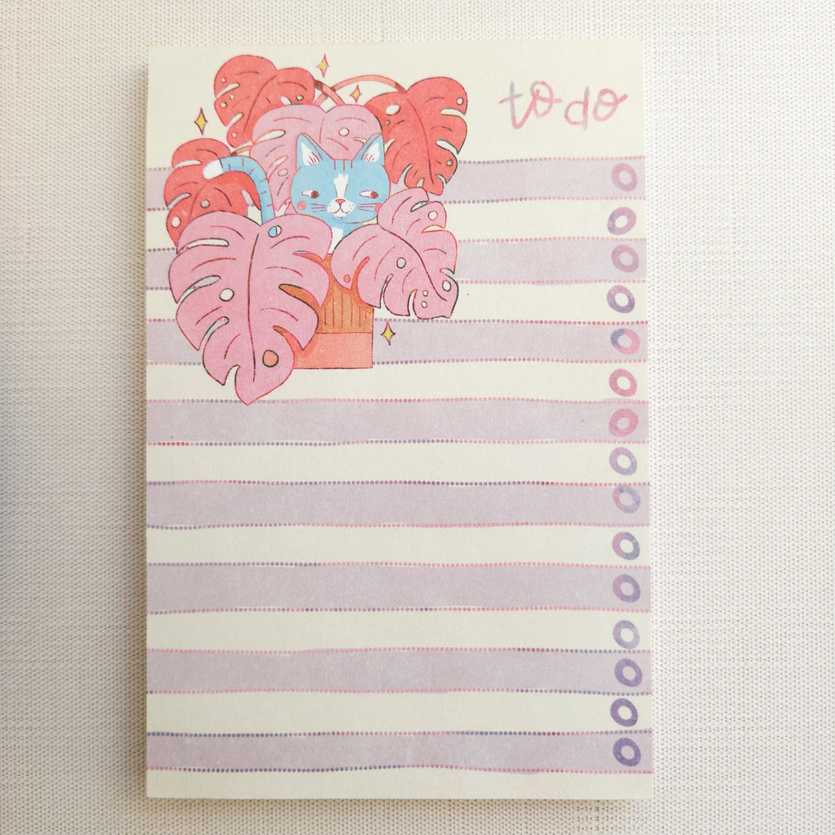 Inside a cozy Wildflower Woods cottage, a curious cat lounges among broad monstera leaves, tucked into a corner filled with filtered light and trailing greenery. This notepad brings that leafy, lived-in moment to your desk, making everyday lists feel a little more inviting.

Designed to be practical without feeling busy, this notepad offers a simple, cheerful way to keep track of daily to-do lists and planning.