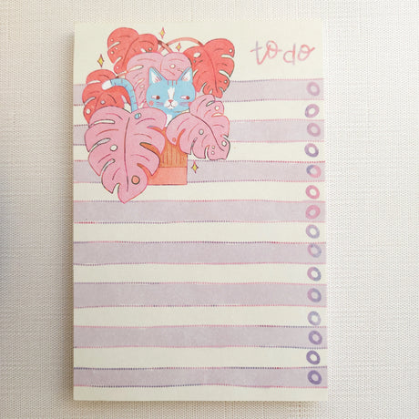 Inside a cozy Wildflower Woods cottage, a curious cat lounges among broad monstera leaves, tucked into a corner filled with filtered light and trailing greenery. This notepad brings that leafy, lived-in moment to your desk, making everyday lists feel a little more inviting.

Designed to be practical without feeling busy, this notepad offers a simple, cheerful way to keep track of daily to-do lists and planning.
