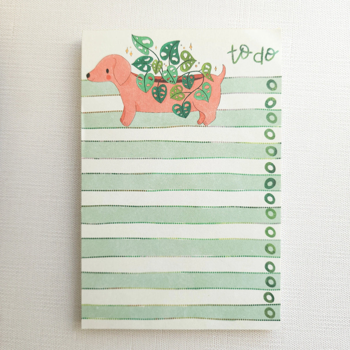 In a sunny Wildflower Woods cottage, a dachshund planter rests near a stack of well-loved books, leafy greens spilling gently from its back. This notepad brings that cozy, decorative moment to your desk, making everyday lists feel a little more inviting.

Designed to be practical without feeling busy, this notepad offers a simple, cheerful way to keep track of daily to-do lists and planning.