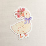 A sweet goose pauses with a bouquet of flowers held gently in its beak, a blue bow tied neatly at its neck. This vinyl sticker captures that charming, flower-filled moment, adding a warm, cottage-inspired touch to your everyday essentials.

Made from durable, waterproof vinyl, this sticker is designed to hold up wherever you place it—whether that’s a water bottle, laptop, or journal you reach for daily.