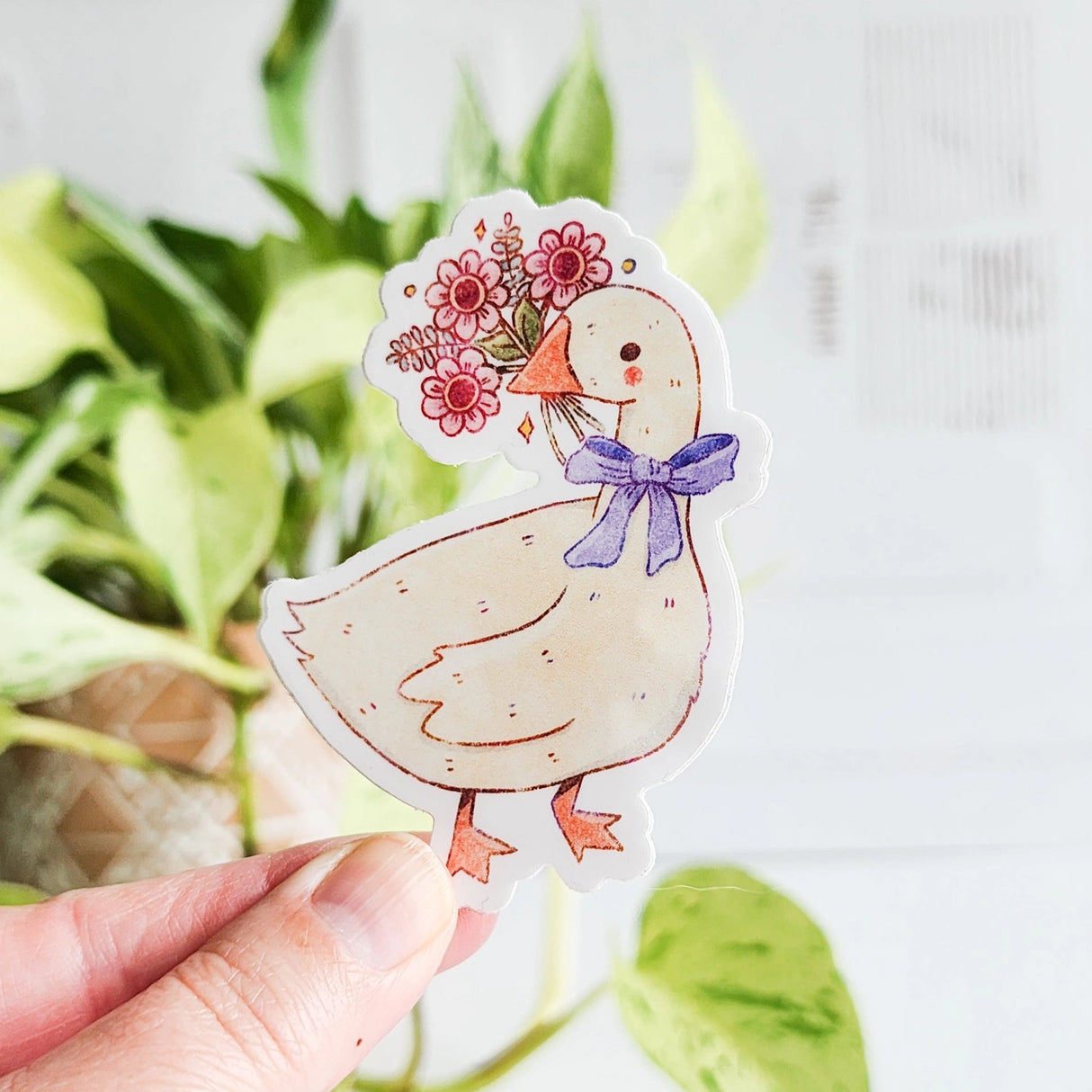 A sweet goose pauses with a bouquet of flowers held gently in its beak, a blue bow tied neatly at its neck. This vinyl sticker captures that charming, flower-filled moment, adding a warm, cottage-inspired touch to your everyday essentials.

Made from durable, waterproof vinyl, this sticker is designed to hold up wherever you place it—whether that’s a water bottle, laptop, or journal you reach for daily.