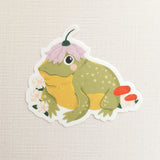 A happy little toad pauses among blooming flowers and mushrooms, a small flower worn proudly atop his head. This vinyl sticker captures that lighthearted moment, celebrating comfort, confidence, and being yourself in the everyday.

Made from durable, waterproof vinyl, this sticker is designed to hold up wherever you place it—whether that’s a water bottle, laptop, or journal you reach for daily.