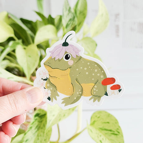 A happy little toad pauses among blooming flowers and mushrooms, a small flower worn proudly atop his head. This vinyl sticker captures that lighthearted moment, celebrating comfort, confidence, and being yourself in the everyday.

Made from durable, waterproof vinyl, this sticker is designed to hold up wherever you place it—whether that’s a water bottle, laptop, or journal you reach for daily.