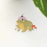 A happy little toad pauses among blooming flowers and mushrooms, a small flower worn proudly atop his head. This vinyl sticker captures that lighthearted moment, celebrating comfort, confidence, and being yourself in the everyday.

Made from durable, waterproof vinyl, this sticker is designed to hold up wherever you place it—whether that’s a water bottle, laptop, or journal you reach for daily.
