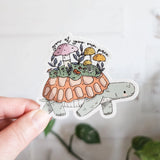 A turtle travels along a mossy path in Wildflower Woods, carrying a tiny mushroom meadow on its back as it moves steadily forward. This vinyl sticker captures that unhurried moment, carrying a gentle reminder that growth happens in its own time.

Made from durable, waterproof vinyl, this sticker is designed to hold up wherever you place it—whether that’s a water bottle, laptop, or journal you reach for daily.