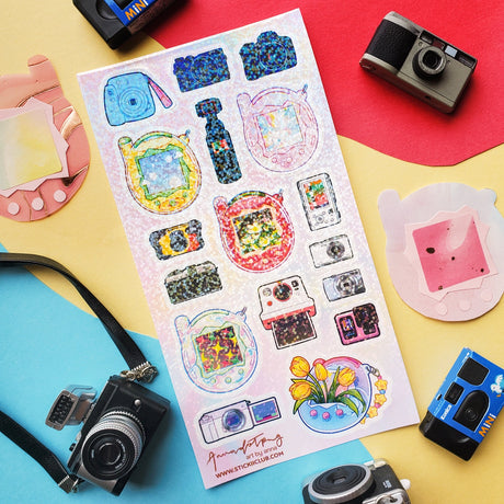 📸✨ Say cheese! From chunky digicams and instant printers to retro film cameras and pocket-sized pixel pets, this snap-happy sheet by @annadotpng is fully loaded with snapshot nostalgia. It’s a shutterbug’s dream, packed with dreamy screens and gadgets that totally flash back. Ready to capture some sticker magic? Point, shoot, print, repeat!

Art by: @annadotpng

Top Coating: Holo Glitter
Adhesive Layer: PVC (plastic)
Backing Layer: Clear PET
6.69" x 3.54".
Weight - 0.03lbs.
1 sheet included &nbsp; &nbsp;