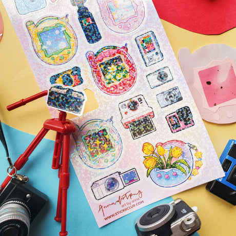 📸✨ Say cheese! From chunky digicams and instant printers to retro film cameras and pocket-sized pixel pets, this snap-happy sheet by @annadotpng is fully loaded with snapshot nostalgia. It’s a shutterbug’s dream, packed with dreamy screens and gadgets that totally flash back. Ready to capture some sticker magic? Point, shoot, print, repeat!

Art by: @annadotpng

Top Coating: Holo Glitter
Adhesive Layer: PVC (plastic)
Backing Layer: Clear PET
6.69" x 3.54".
Weight - 0.03lbs.
1 sheet included &nbsp; &nbsp;